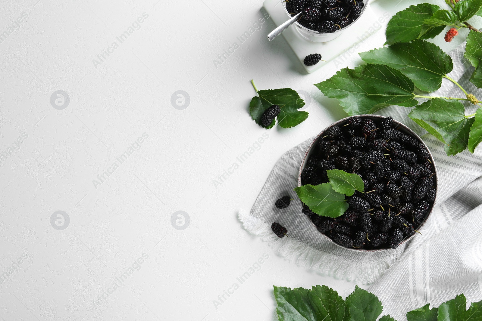 Photo of Bowl of delicious ripe black mulberries on white table, flat lay. Space for text
