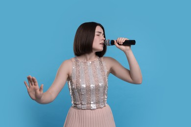 Photo of Beautiful young woman with microphone singing on light blue background