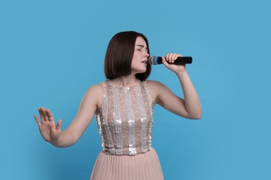 Beautiful young woman with microphone singing on light blue background