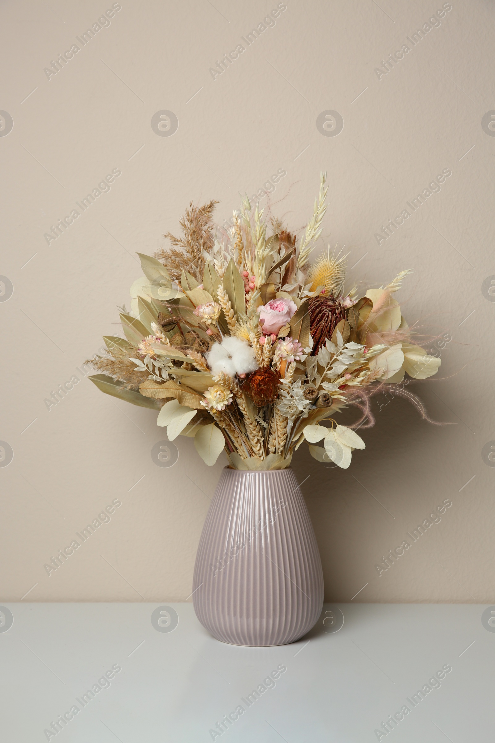 Photo of Beautiful dried flower bouquet in ceramic vase on white table near light grey wall