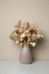 Beautiful dried flower bouquet in ceramic vase on white table near light grey wall