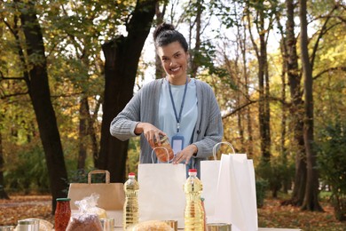 Portrait of volunteer packing food products at table in park