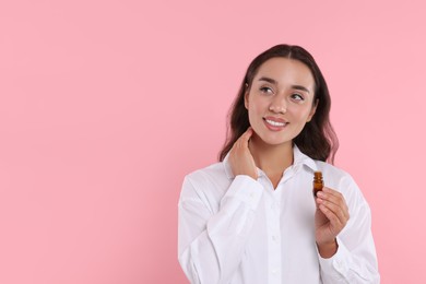 Photo of Beautiful happy woman with bottle of essential oil on pink background, space for text