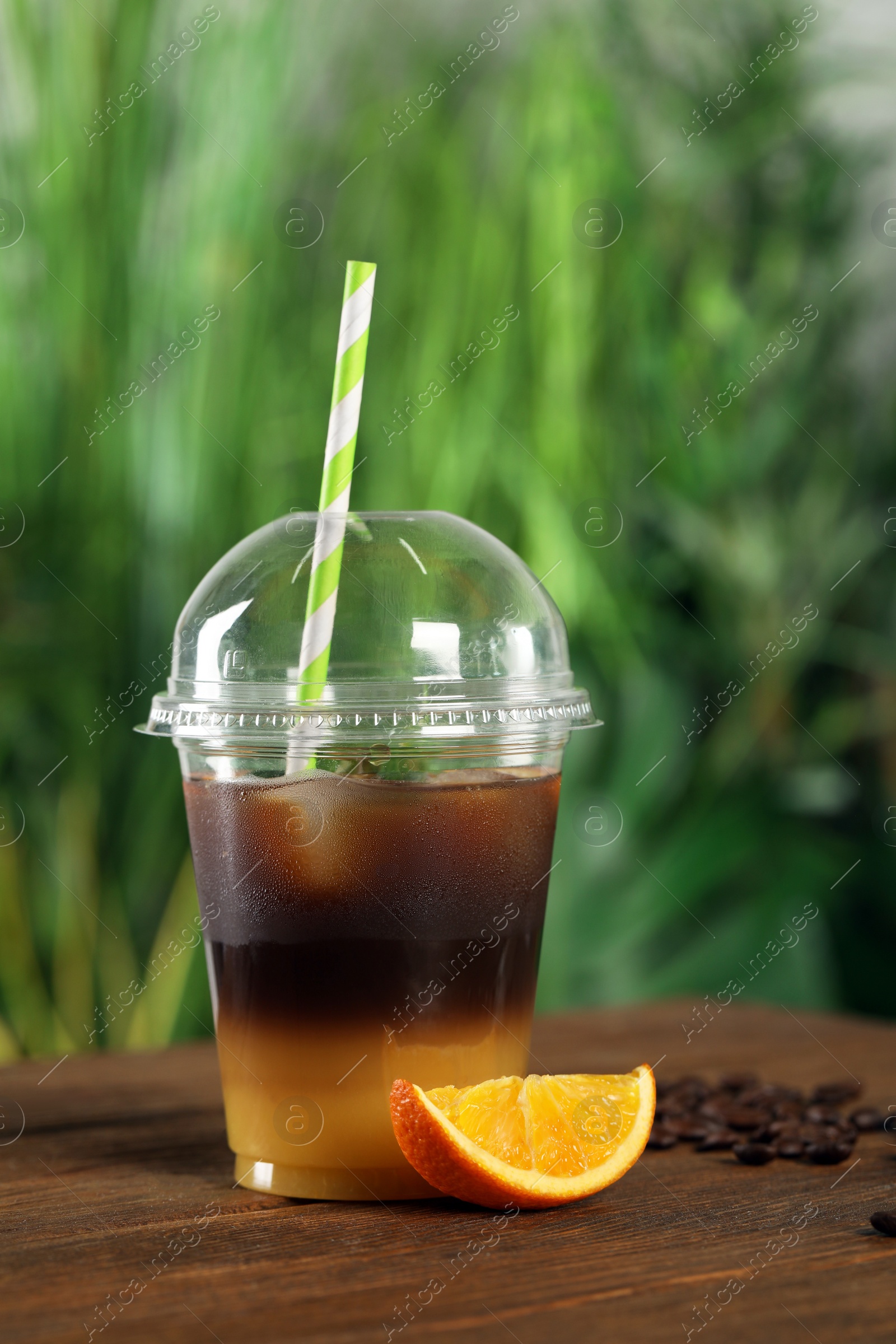 Photo of Tasty refreshing drink with coffee and orange juice in plastic cup on wooden table against blurred background