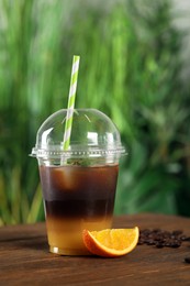 Tasty refreshing drink with coffee and orange juice in plastic cup on wooden table against blurred background