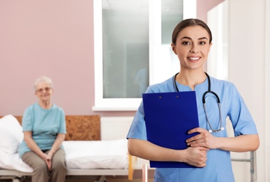 Portrait of nurse with clipboard in senior patient's hospital ward