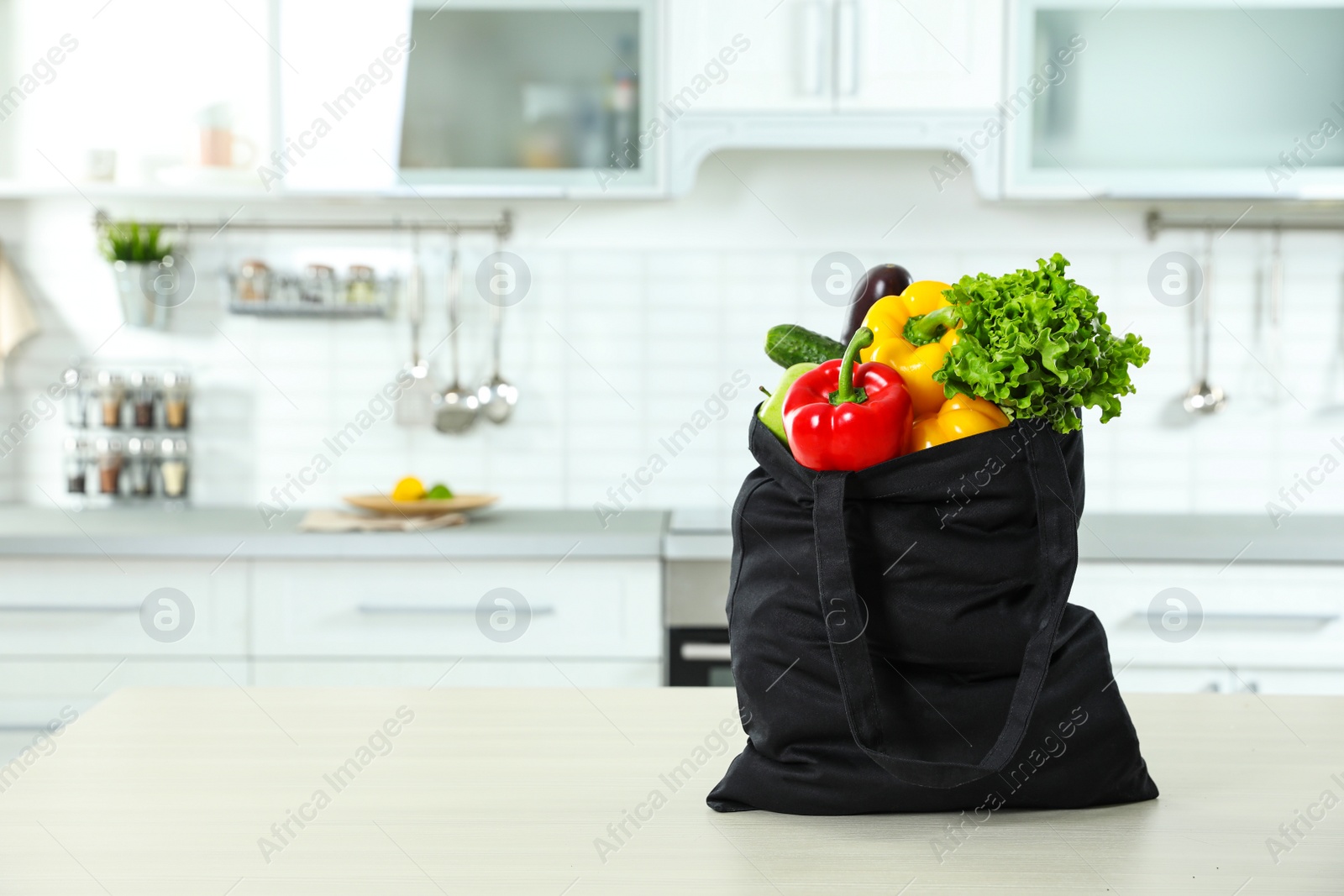 Photo of Textile shopping bag full of vegetables on table in kitchen. Space for text