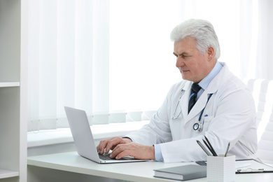 Senior doctor working with laptop at table in office