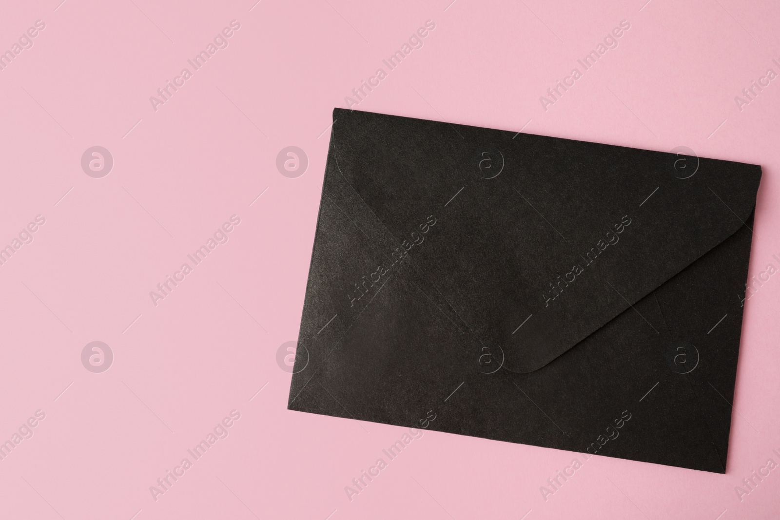 Photo of Black paper envelope on pink background, top view. Space for text