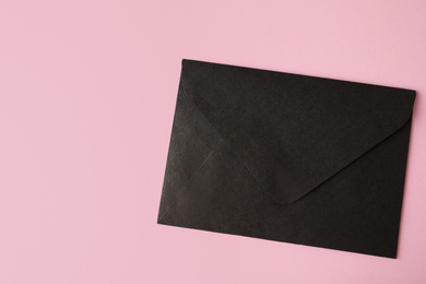 Photo of Black paper envelope on pink background, top view. Space for text