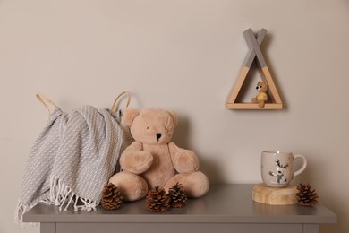 Photo of Teddy bear, conifer cones and drink on table in baby room. Interior design