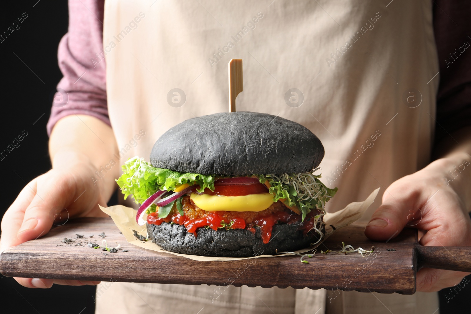 Photo of Woman holding board with tasty black vegetarian burger, closeup