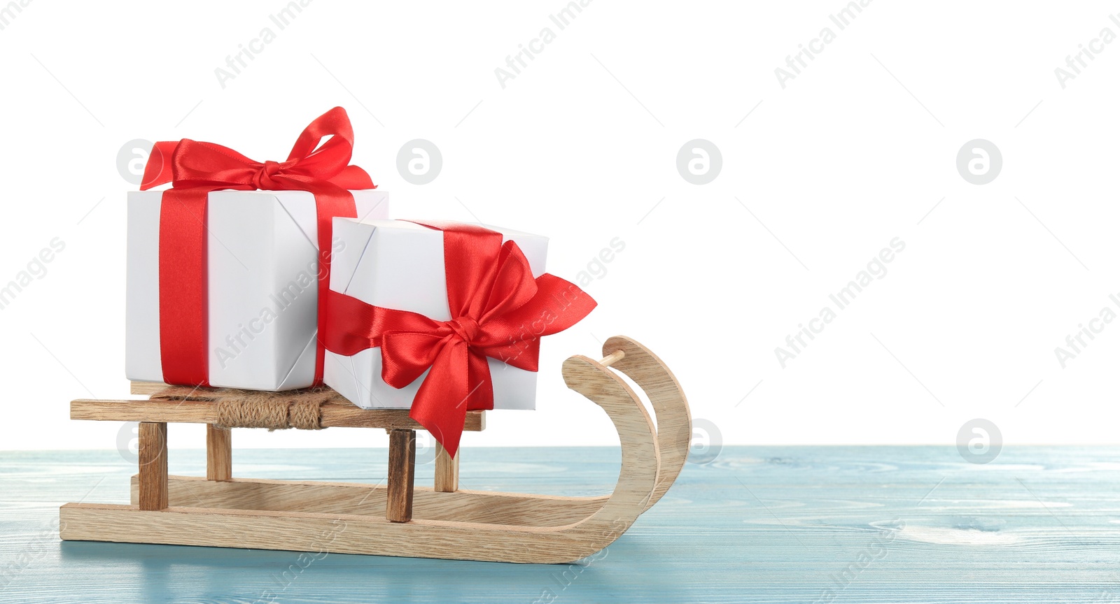Photo of Decorative sleigh with Christmas gift boxes on light blue wooden table. Space for text