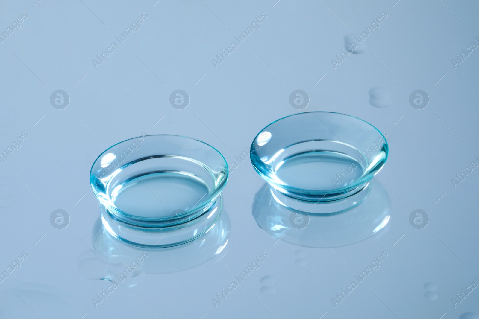 Photo of Pair of contact lenses on wet light blue reflective surface