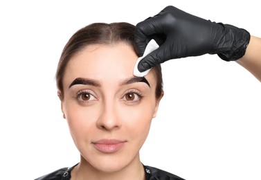 Photo of Beautician wiping tint from woman's eyebrows on white background, closeup