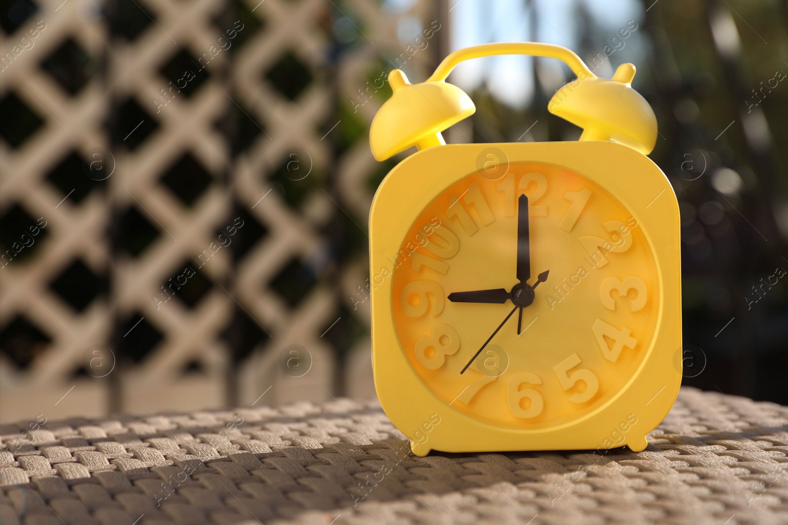 Photo of Yellow alarm clock on table outdoors at sunny morning. Space for text