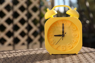Photo of Yellow alarm clock on table outdoors at sunny morning. Space for text