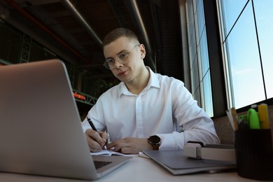 Young male student with laptop studying at table in cafe