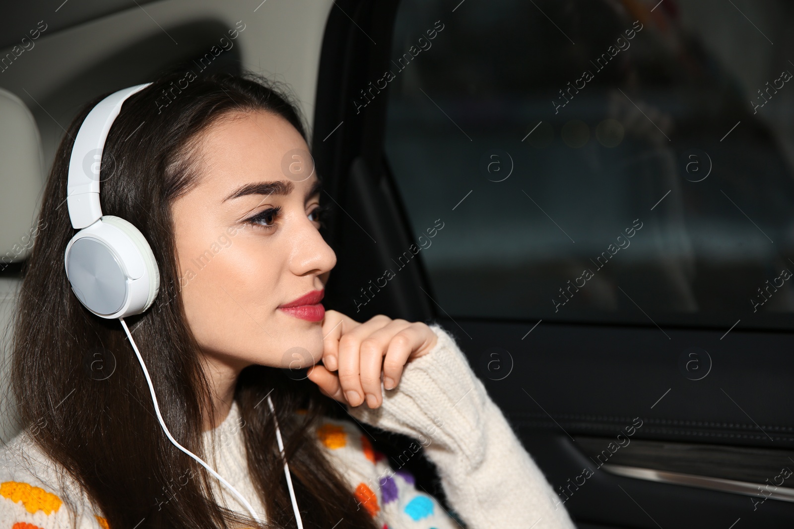 Photo of Beautiful young woman listening to music with headphones in car. Space for text