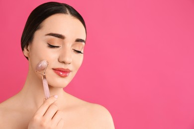 Photo of Woman using natural face roller on pink background, space for text