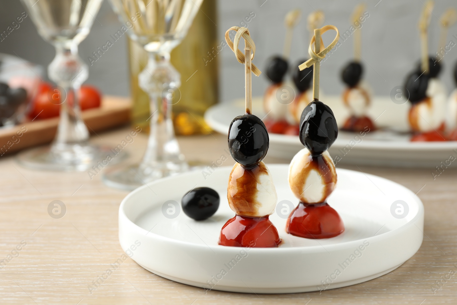 Photo of Tasty canapes with black olives, mozzarella and cherry tomatoes on light wooden table, closeup