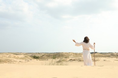 Photo of Jesus Christ raising hand in desert, back view. Space for text
