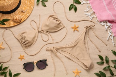 Stylish bikini and beach accessories on sand, flat lay