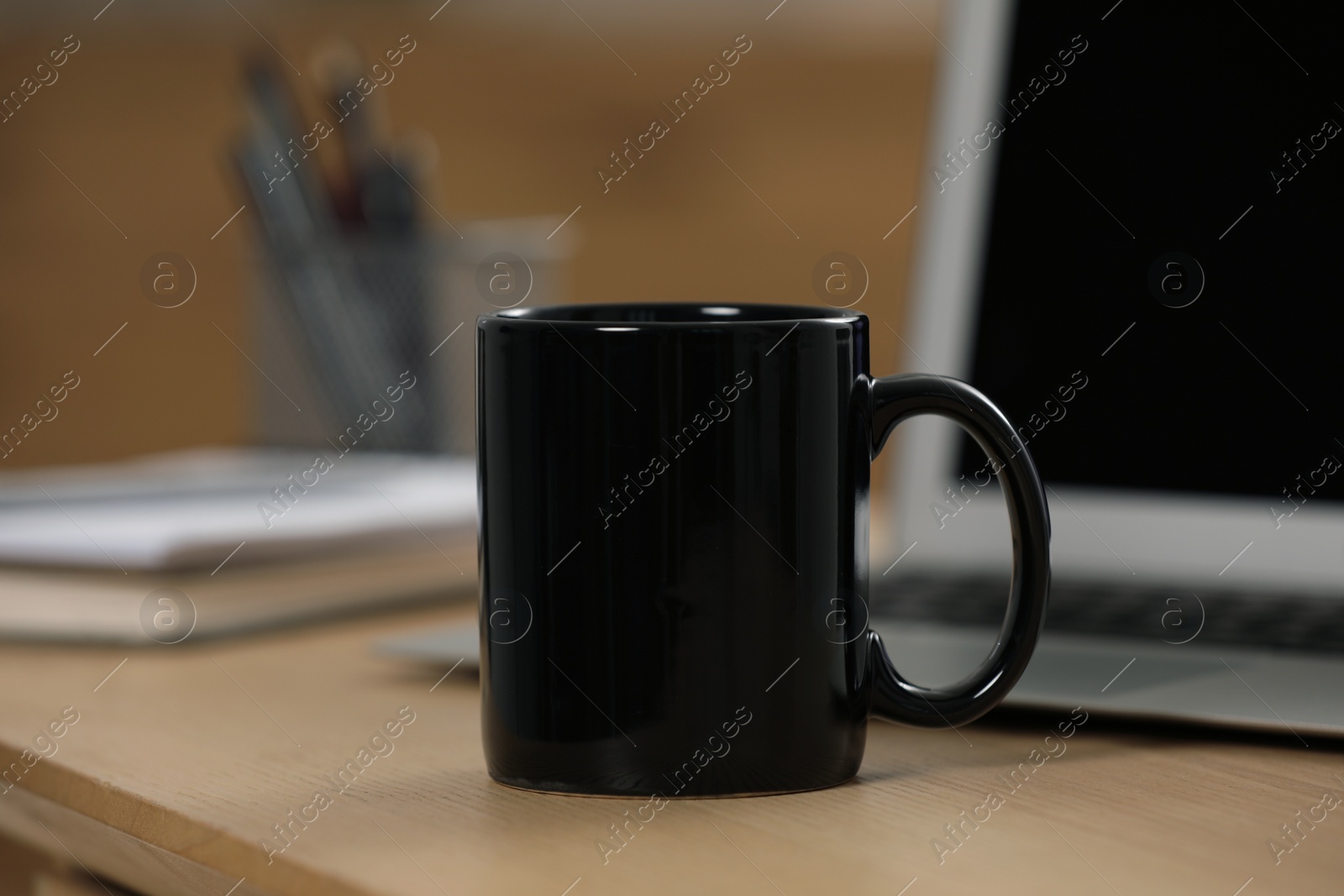 Photo of Black ceramic mug and laptop on wooden table at workplace