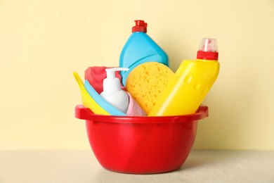 Photo of Basin with different cleaning supplies on light floor near beige wall