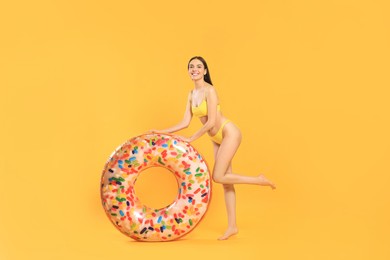 Happy young woman with beautiful suntan and inflatable ring against orange background