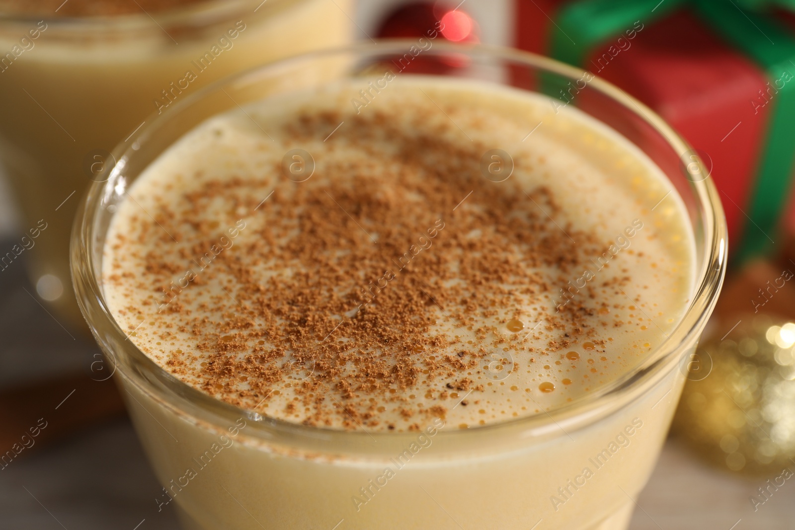Photo of Tasty eggnog with cinnamon in glass on table, closeup