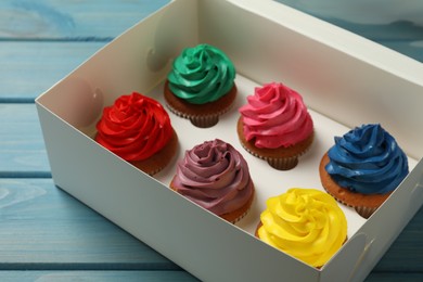 Photo of Box with different cupcakes on light blue wooden table, closeup