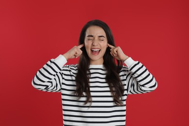 Photo of Emotional young woman covering ears with fingers on red background