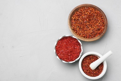 Photo of Kitchenware with chili pepper flakes on light background, top view