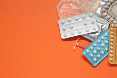 Contraceptive pills, condoms and intrauterine device on orange background, flat lay with space for text. Different birth control methods
