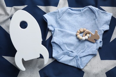 Photo of Rocket shaped child's night lamp, baby bodysuit and rattle on color fabric, flat lay