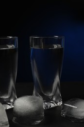 Photo of Shot glassvodka with ice cubes on black table against dark background, closeup