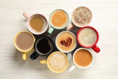 Photo of Many cups with different aromatic coffee on white wooden table, flat lay