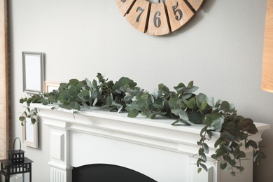 Photo of Beautiful garland with eucalyptus branches on mantelpiece in room