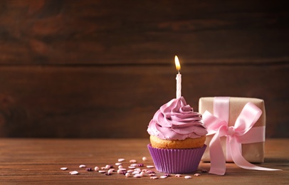 Photo of Gift box and delicious birthday cupcake with candle on table