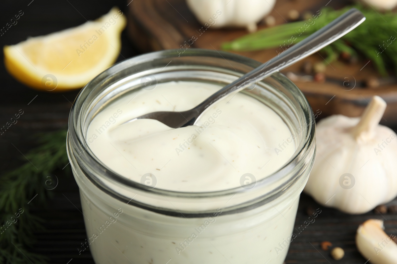 Photo of Jar of garlic sauce with spoon on table, closeup