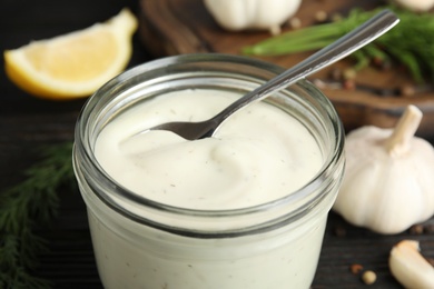 Photo of Jar of garlic sauce with spoon on table, closeup