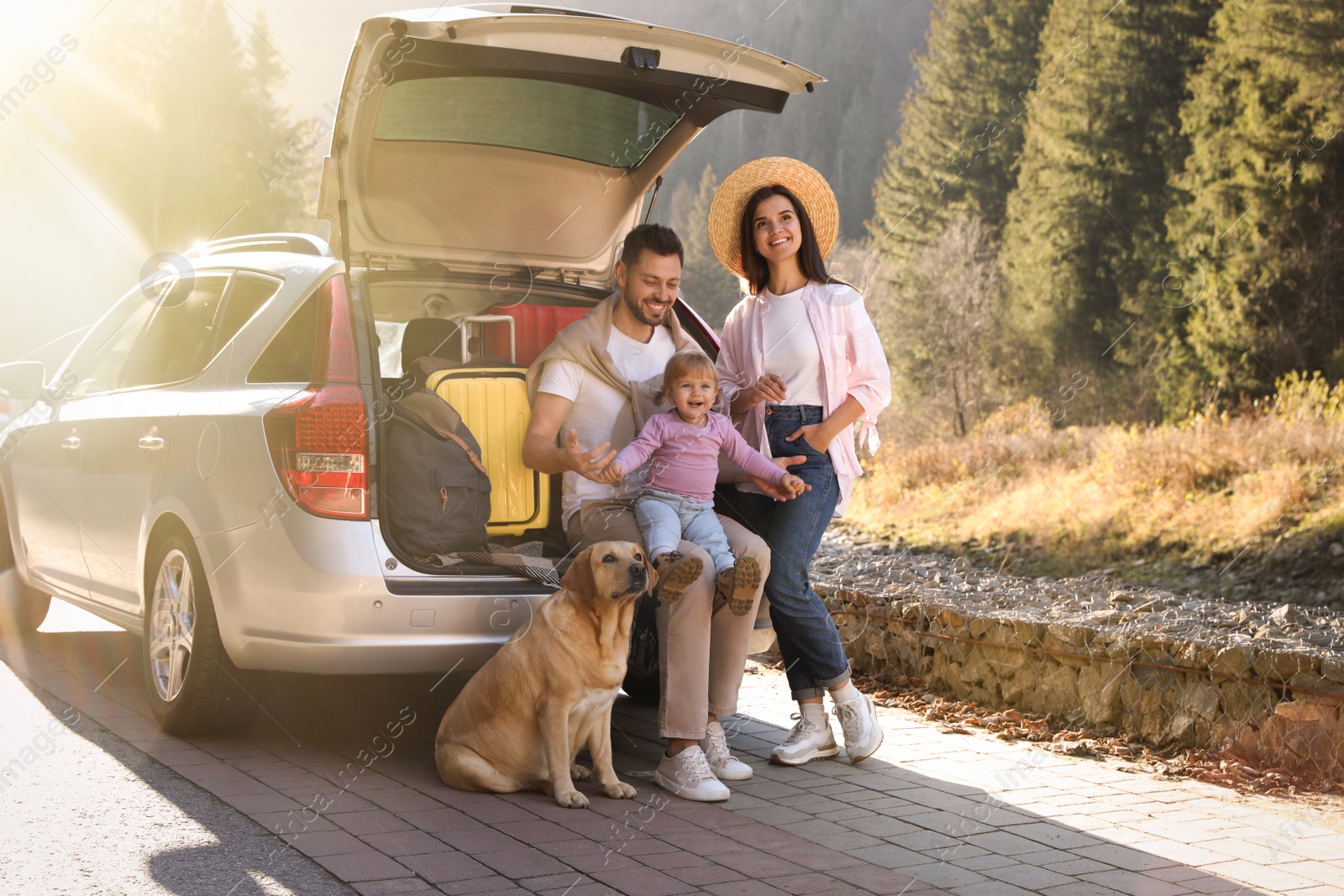 Photo of Parents, their daughter and dog near car outdoors. Family traveling with pet