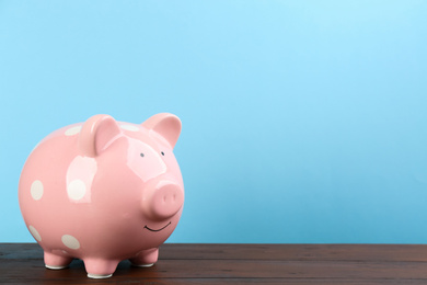 Photo of Pink piggy bank on wooden table against light blue background. Space for text
