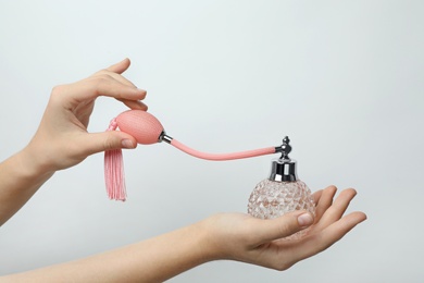 Woman holding perfume bottle on light background, closeup