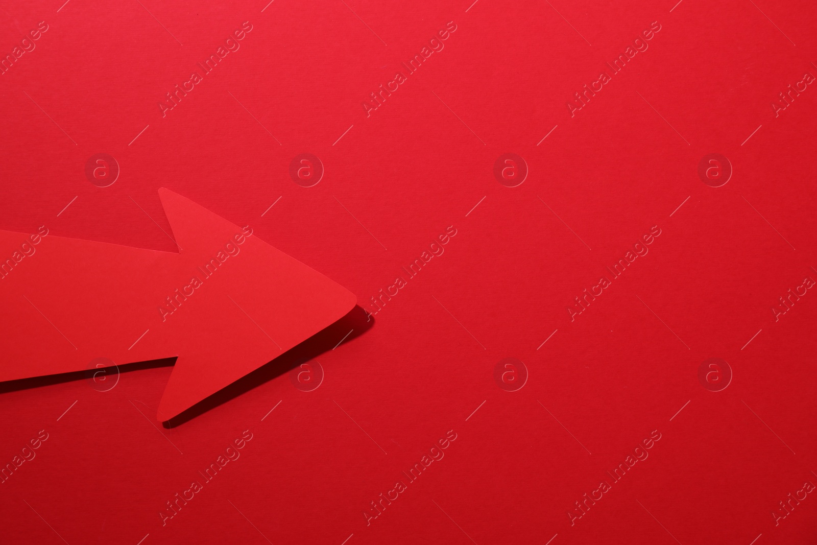 Photo of One paper arrow on red background, top view. Space for text