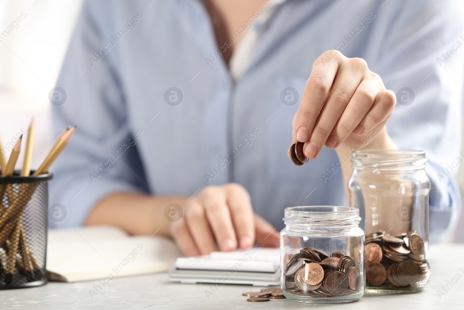 Photo of Woman putting money into glass jar at table, closeup