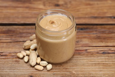 Tasty nut paste in jar and peanuts on wooden table, closeup