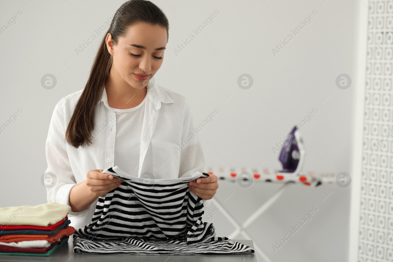 Photo of Young woman folding clothes at grey table indoors