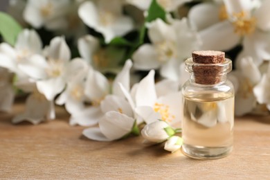 Photo of Jasmine essential oil and fresh flowers on wooden table, space for text